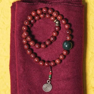 Bodhi seed cyan jade copper bracelet flat lay with double wrap design and spiral metal pendant on maroon fabric