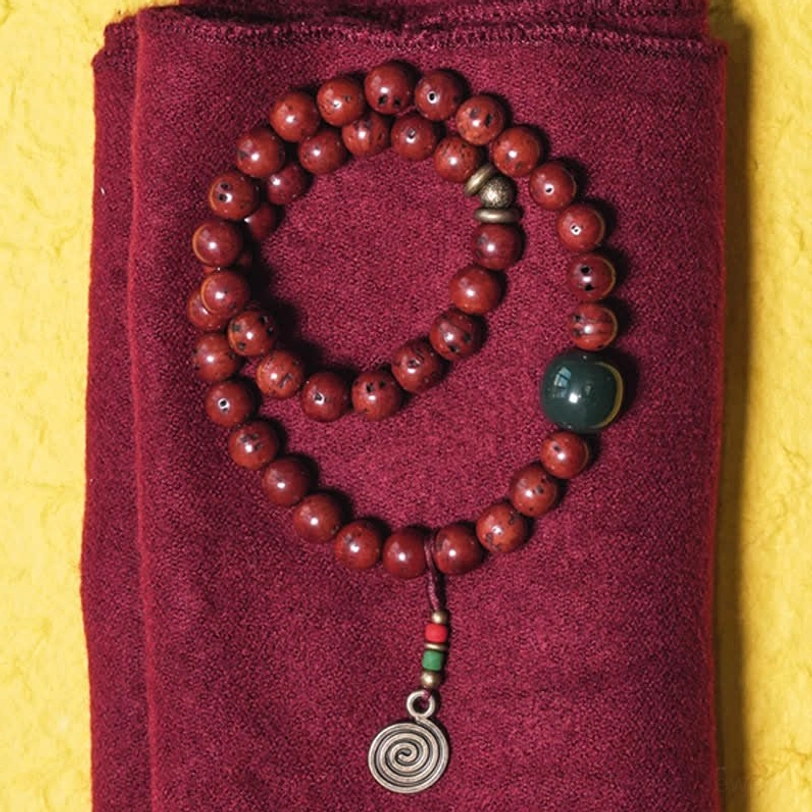 Bodhi seed cyan jade copper bracelet flat lay with double wrap design and spiral metal pendant on maroon fabric
