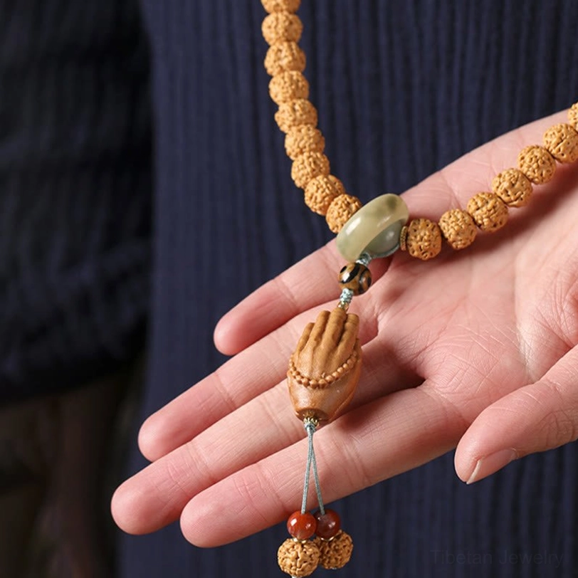 Hand-held Bodhi seed prayer bracelet with three-eye Dzi bead and jade accessory beads against dark garment background