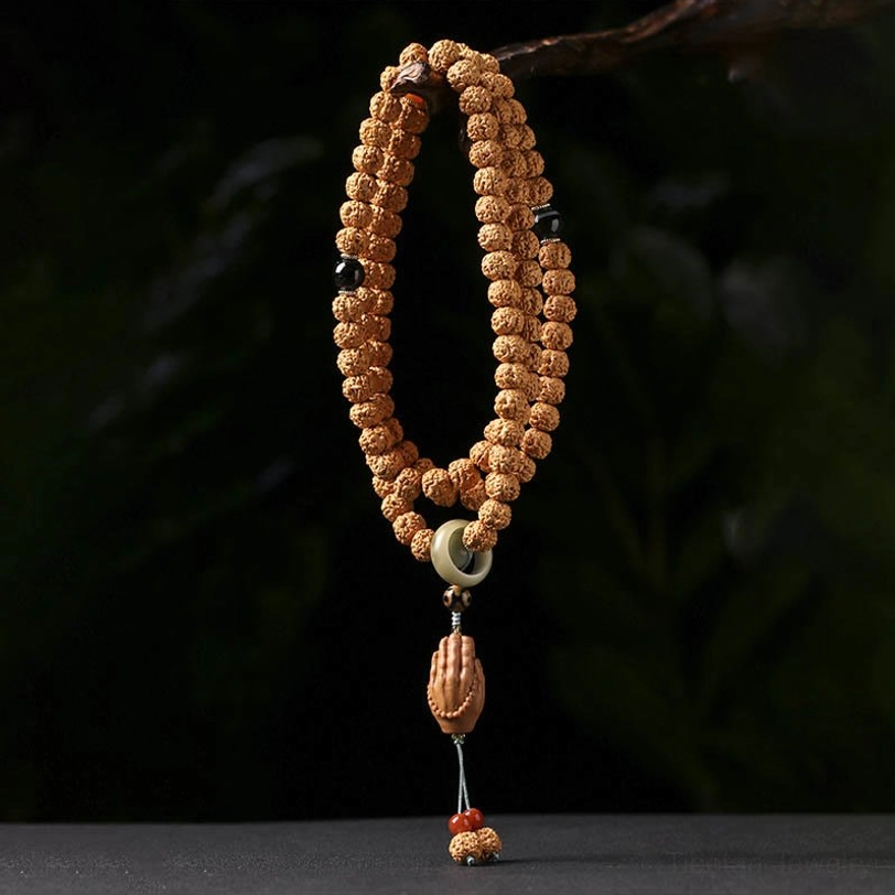 Coiled Bodhi seed prayer bracelet with three-eye Dzi bead and wooden Buddha hand charm pendant on dark green background
