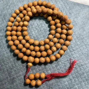 108 Bodhi seed mala beads bracelet with red tassel displayed on grey quilted fabric, light brown natural seeds
