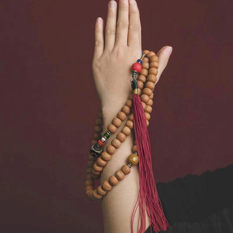 Bodhi seed mala bracelet close-up handheld against dark red background, highlighting bead patterns and tassel