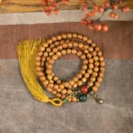 108 Bodhi seed mala bracelet flat lay with mustard tassel, jade and cinnabar accent beads on cloth background