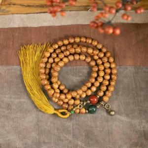 108 Bodhi seed mala bracelet flat lay with mustard tassel, jade and cinnabar accent beads on cloth background