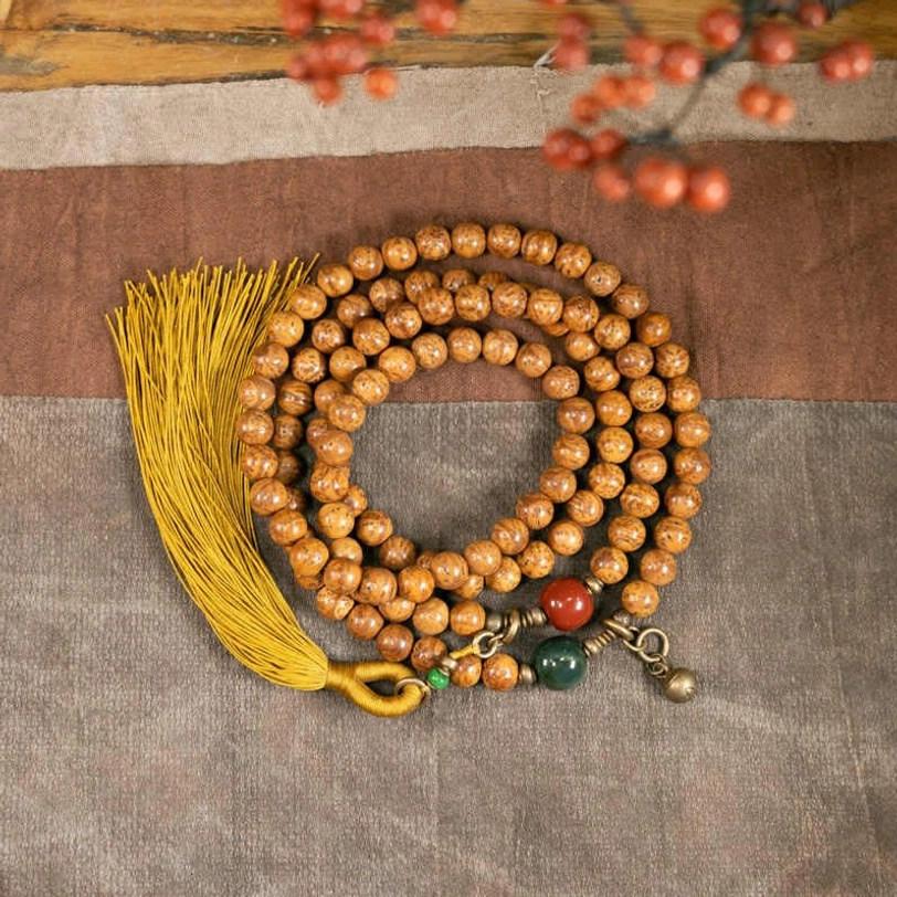 108 Bodhi seed mala bracelet flat lay with mustard tassel, jade and cinnabar accent beads on cloth background
