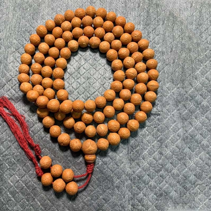 Complete 108 Bodhi seed mala bracelet with medium brown beads and red fabric tassel pendant on grey background