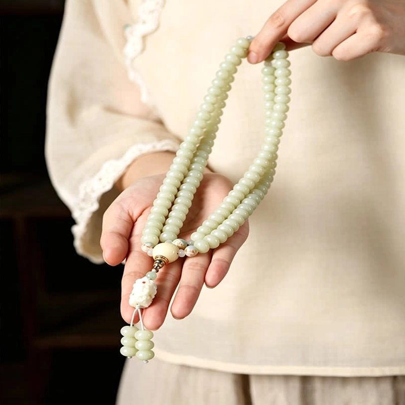 White bodhi seed mala held in human hands close-up showing carved pendant and natural bead texture