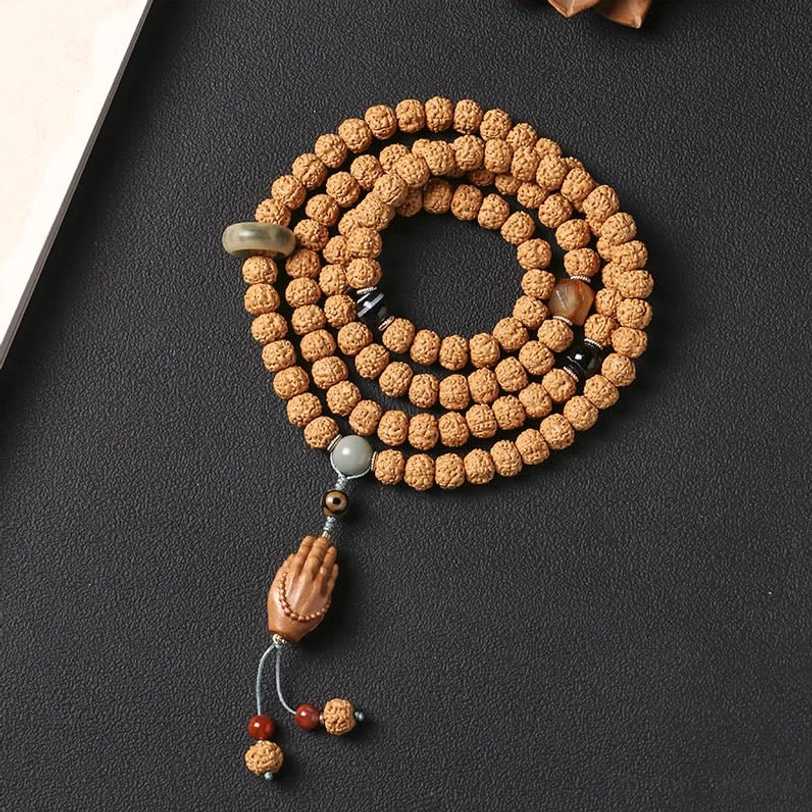 Top-down view of Bodhi seed mala bracelet with jade ring, three-eye Dzi bead, and Buddha hand tassel on dark desktop