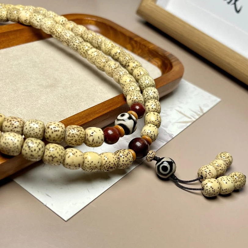 Side view of 108 Bodhi seed mala bracelet with prominent Dzi bead and decorative tassel on display tray