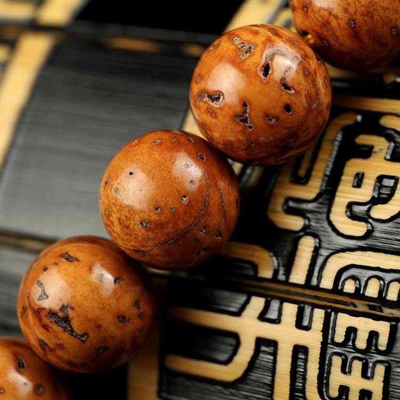 Low-angle close-up of bodhi seeds on carved wooden background, highlighting natural porous tan-brown surface and authentic round bead shape