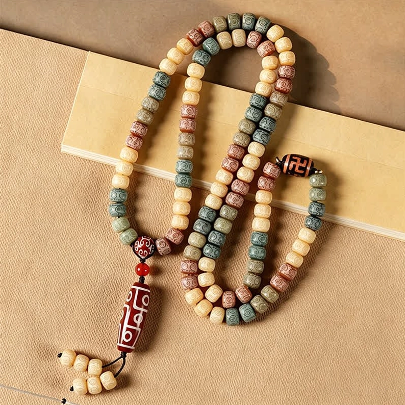 Tibetan bodhi seed mala 108 beads with mixed earth tones and dzi bead pendant with bead tassel on light paper backdrop