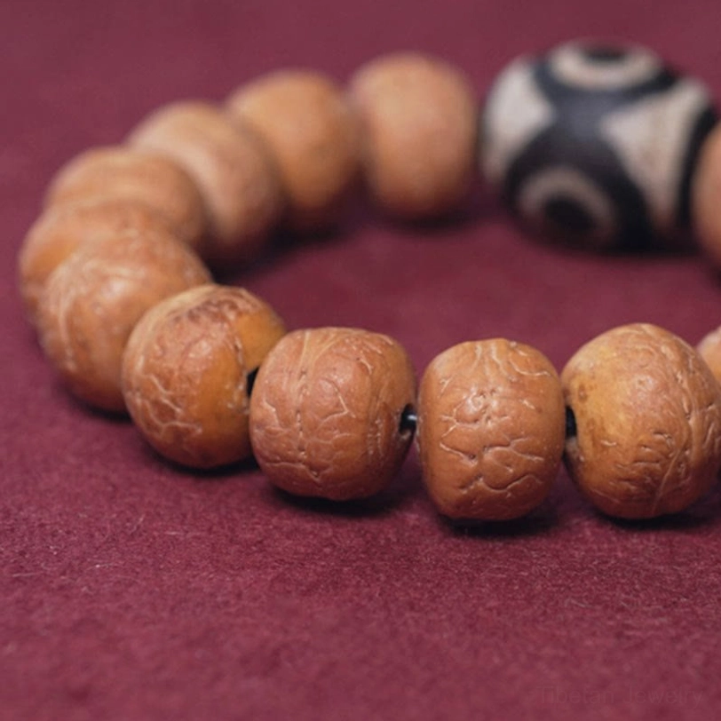 Top-down close-up of natural cracked bodhi bead texture with three-eyed dzi focal bead on wine-red background