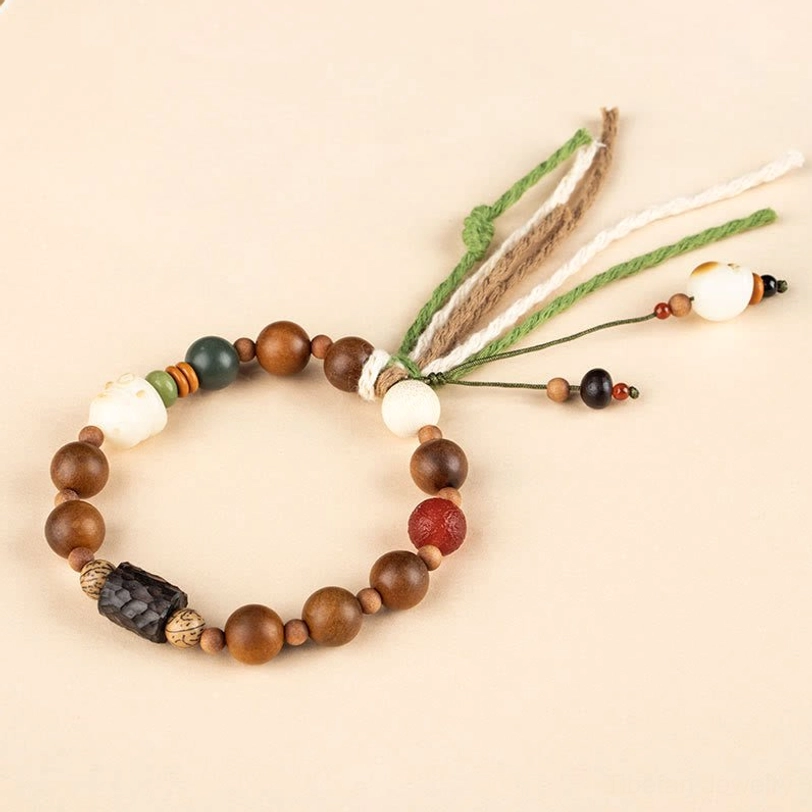 Natural wooden beaded tassel bracelet with brown beads, small green spacers, and mixed fabric tassel on light beige background