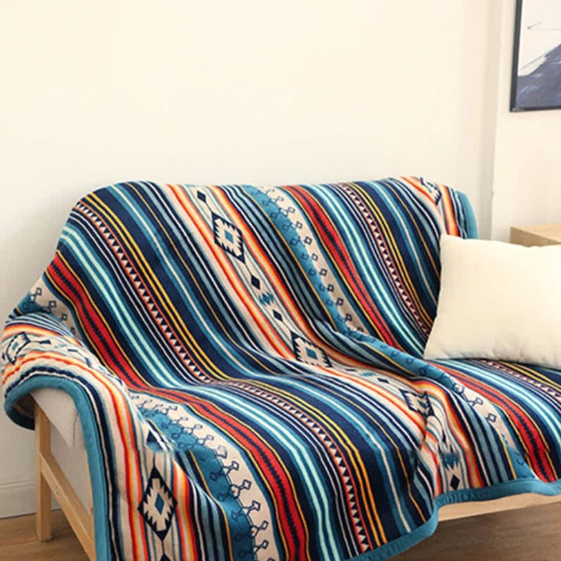Tibetan-inspired throw blanket flat lay on sofa featuring vibrant boho stripe print and neat blue border, small living room setting