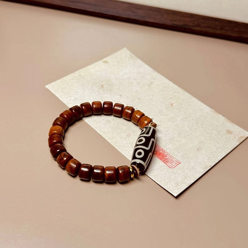 Reddish brown bone Dzi bracelet with patterned nine-eye bead on craft paper