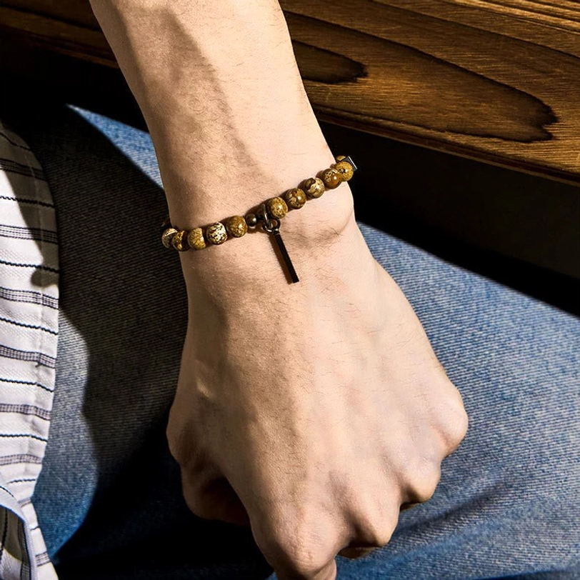 Close-up side view of stone bracelet worn on wrist, slim copper hardware in indoor wooden setting