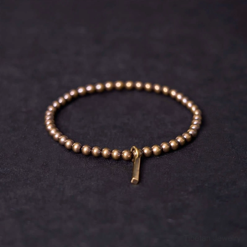 Close-up top view of antique brass beaded bracelet with metal bar charm on grey background