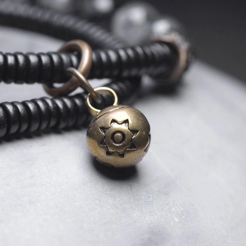 Engraved brass bell charm and black disc beads showing metal fittings and jump rings