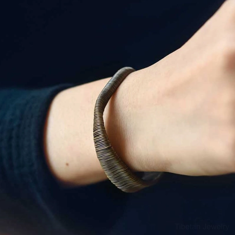 Side close-up view of wrapped brass cuff bracelet showing flat wire panel and looped open end on dark wooden surface