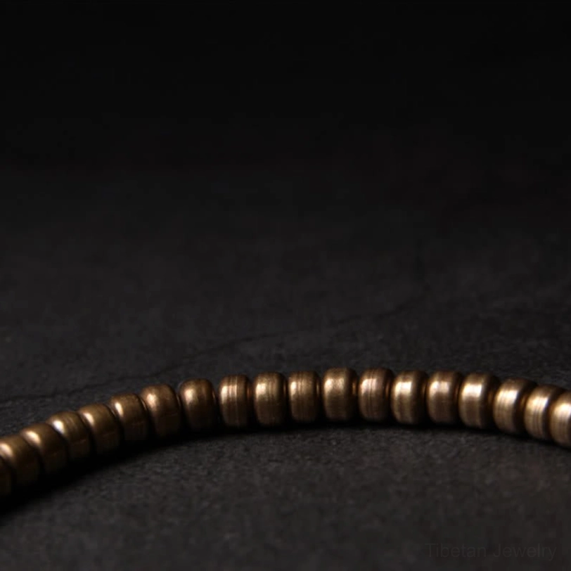 Beaded brass abundance bracelet with uniform cylindrical spacer beads, showing side macro view and subtle bronze aging