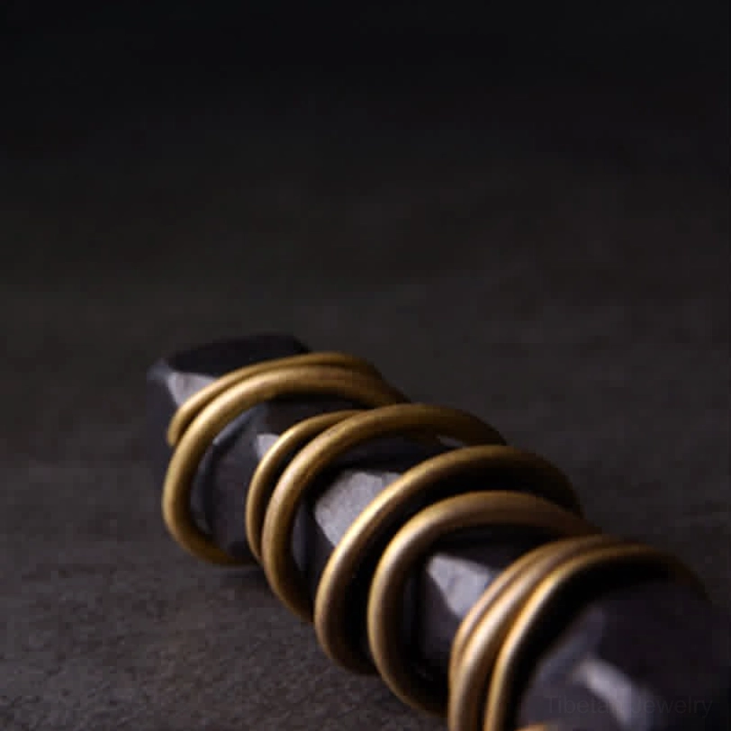 Extreme close-up of layered brass wire coils on Tibetan ebony wood necklace, showing polished brass finish and metal craftsmanship