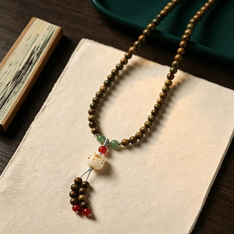 Brown-green sandalwood mala bracelet showing color transition with green accent beads and cat charm on rice paper background