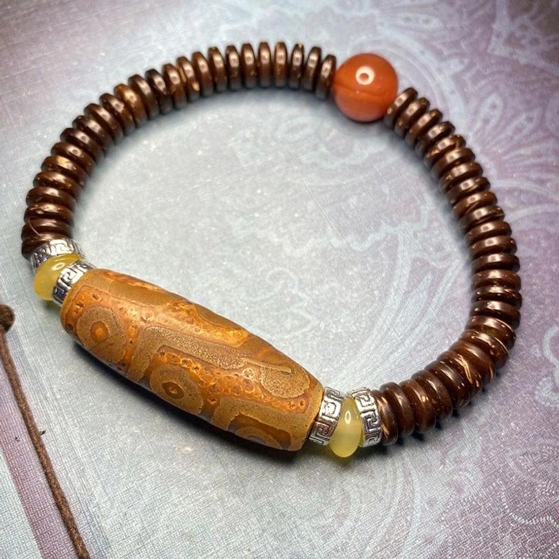 Brown nine-eye dzi bead bracelet with red agate accent bead, turquoise and metal spacers on light purple background