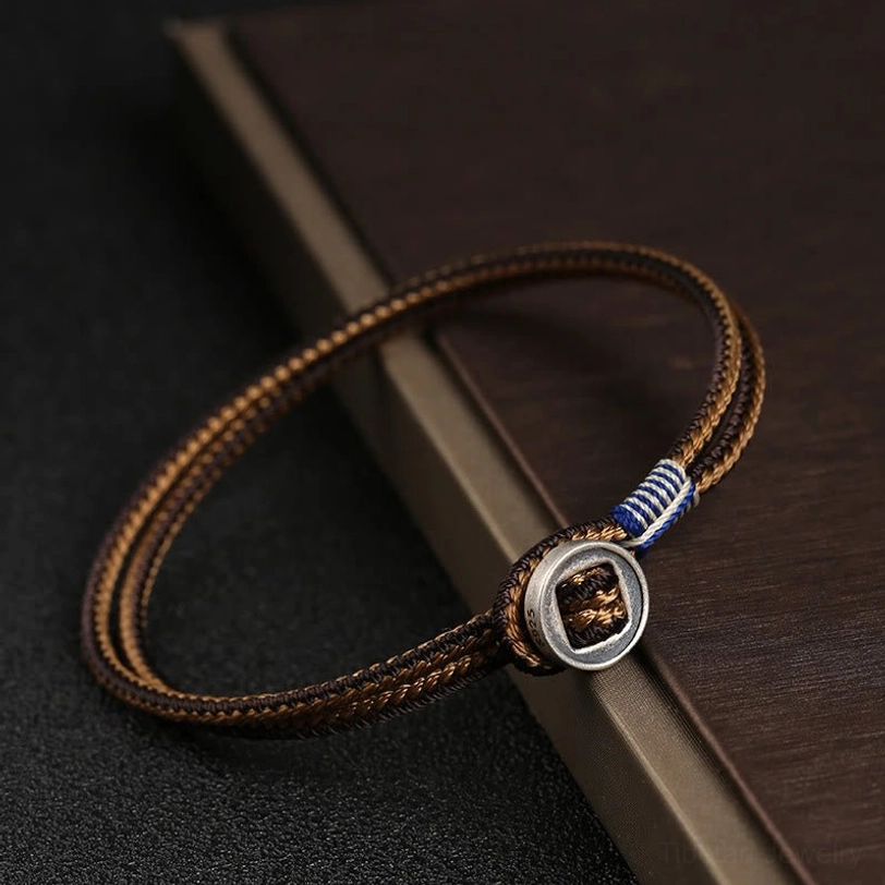 Brown woven tibetan bracelet with blue accent cord and silver round buckle clasp on dark wooden board
