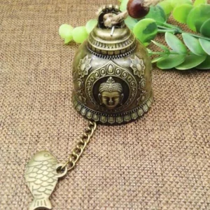Close-up Buddha face embossed bronze wind chime bell with sacred motif and traditional fish charm pendant on jute fabric background