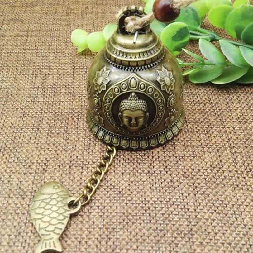 Close-up Buddha face embossed bronze wind chime bell with sacred motif and traditional fish charm pendant on jute fabric background