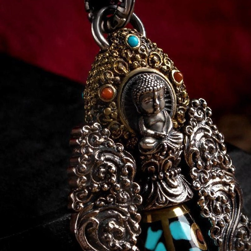 Buddha head detail of Tibetan dzi pendant in front close-up view, showing small seated Buddha sculpture with inlaid turquoise and red gem accents