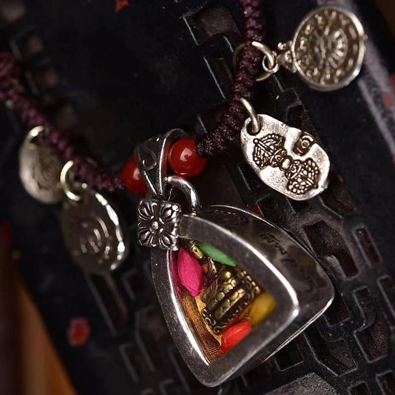 Detailed view of Medicine Buddha necklace charm set displaying multiple engraved silver-toned amulets and triangular buddha pendant on carved wooden surface