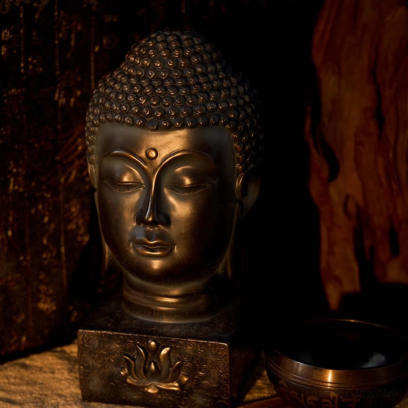 Aged bronze Buddha head statue with lotus emboss detail on base, low perspective view with warm ambient lighting on tabletop
