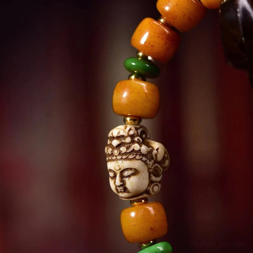 Macro close-up of carved multi-faced buddha bead with green spacer and aged amber camel bone barrel beads - spiritual craftsmanship detail