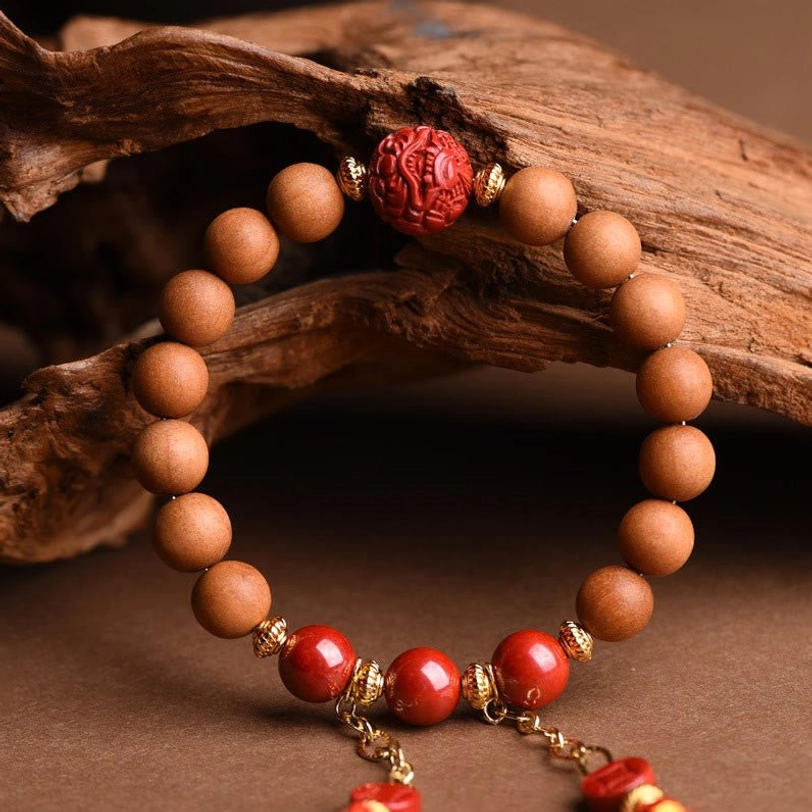 Detailed close-up of hand-carved red cinnabar pixiu focal bead with smooth tan peach wood beads and gold metal fittings on weathered wood