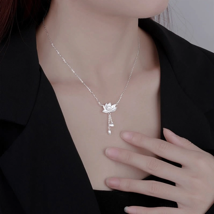 Hand-held detail view of carved silver lotus pendant with tassel charms on wooden display surface