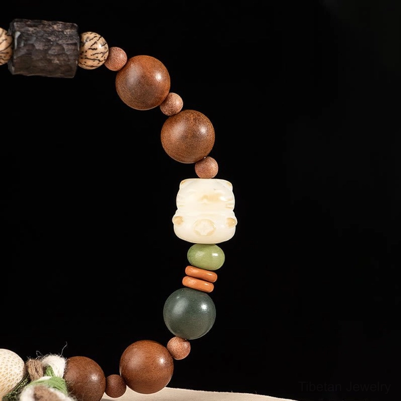 Close-up of carved dark bead and cat paw ornament on lightning strike wood bracelet with green and red accent beads on black background