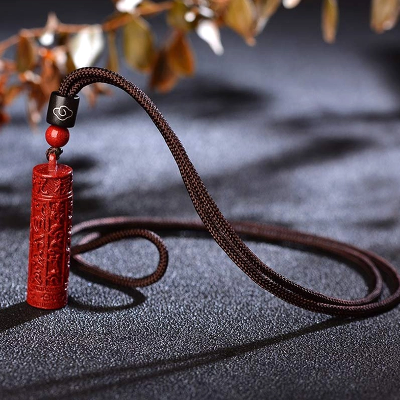 Handcrafted cinnabar amulet pendant with natural stone texture on dark fabric with foliage background
