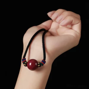 Cinnabar bead blessing necklace hand-held display featuring red stone pendant with multicolored Tibetan braided knots on dark background