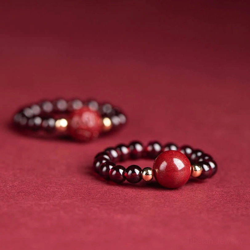 Two styles of cinnabar beaded rings with different protective charms and gold metal spacers on deep red background