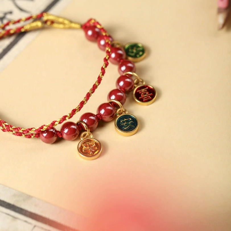 Side angle close-up of cinnabar blessing bracelet showing red-gold braided cord and dangling protective charm pendants