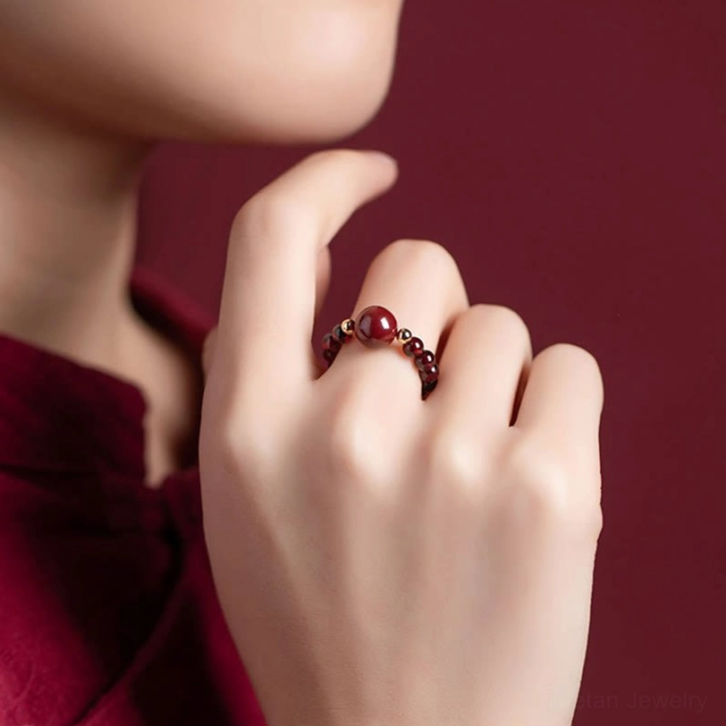 Beaded protection ring with small cinnabar charms and gold metal accents, close-up side view on wine red background