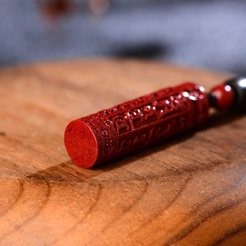 Close-up side view of engraved red cinnabar cylinder pendant with red accent bead on wooden surface
