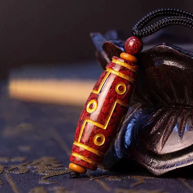 Cinnabar nine-eye dzi bead necklace pendant close-up showing gold inlaid patterns and black braided rope on antique wooden surface