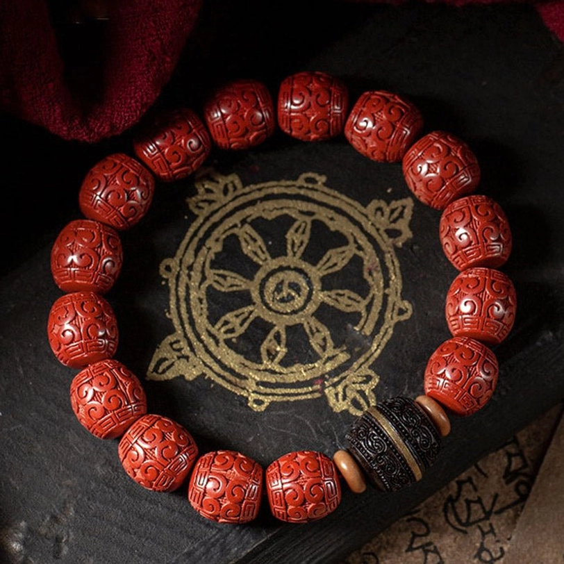 Cinnabar and ebony wooden blessing bracelet displayed on Buddhist scripture mat, showing carved red barrel beads with black ebony spacer beads from overhead view