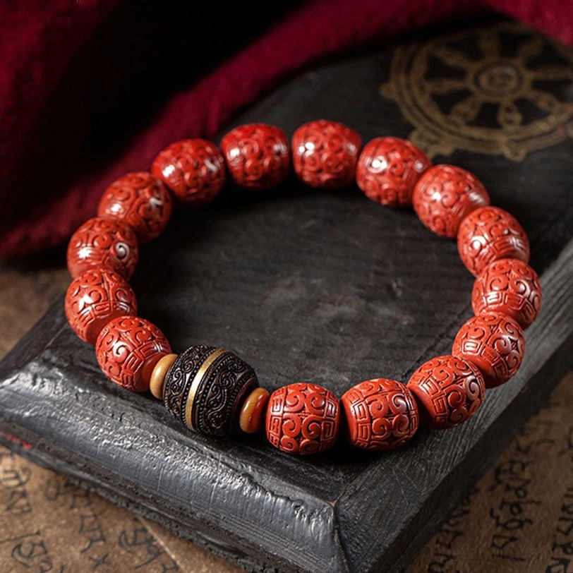 Handcrafted cinnabar prayer beads bracelet flat lay on dark wooden tray with red cloth, featuring embossed red beads and gold-toned metal spacers