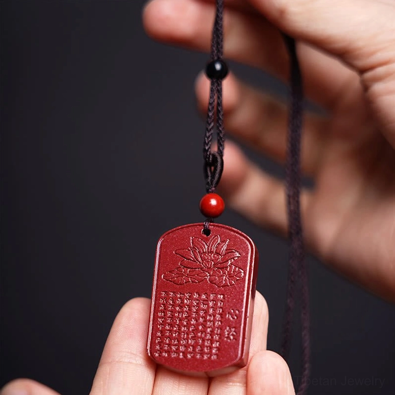Hand-held cinnabar Heart Sutra pendant close-up showing detailed carving of sacred Sanskrit text and lotus symbol