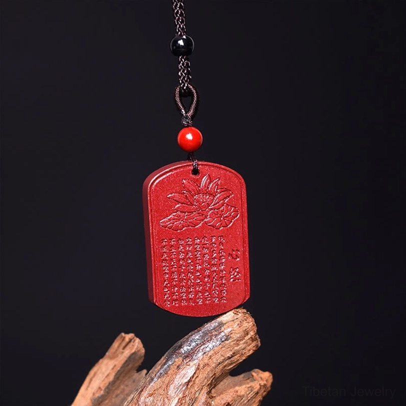 Tibetan cinnabar Heart Sutra pendant necklace hanging vertically with black beaded cord and red accent bead on wooden background