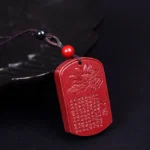 Cinnabar Lotus Heart Sutra pendant necklace close-up overhead view showing hand-carved red stone with lotus design and sacred Sanskrit text on dark background