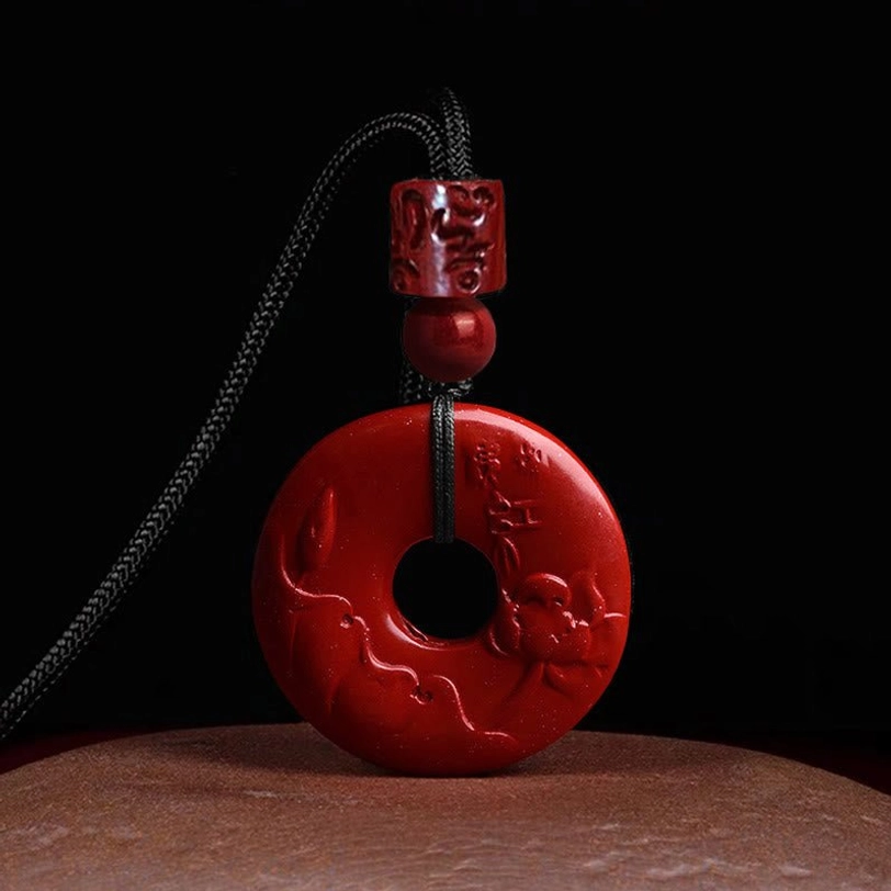 Cinnabar lotus peace buckle pendant with hand-carved lotus design on smooth red surface with adjustable black braided cord